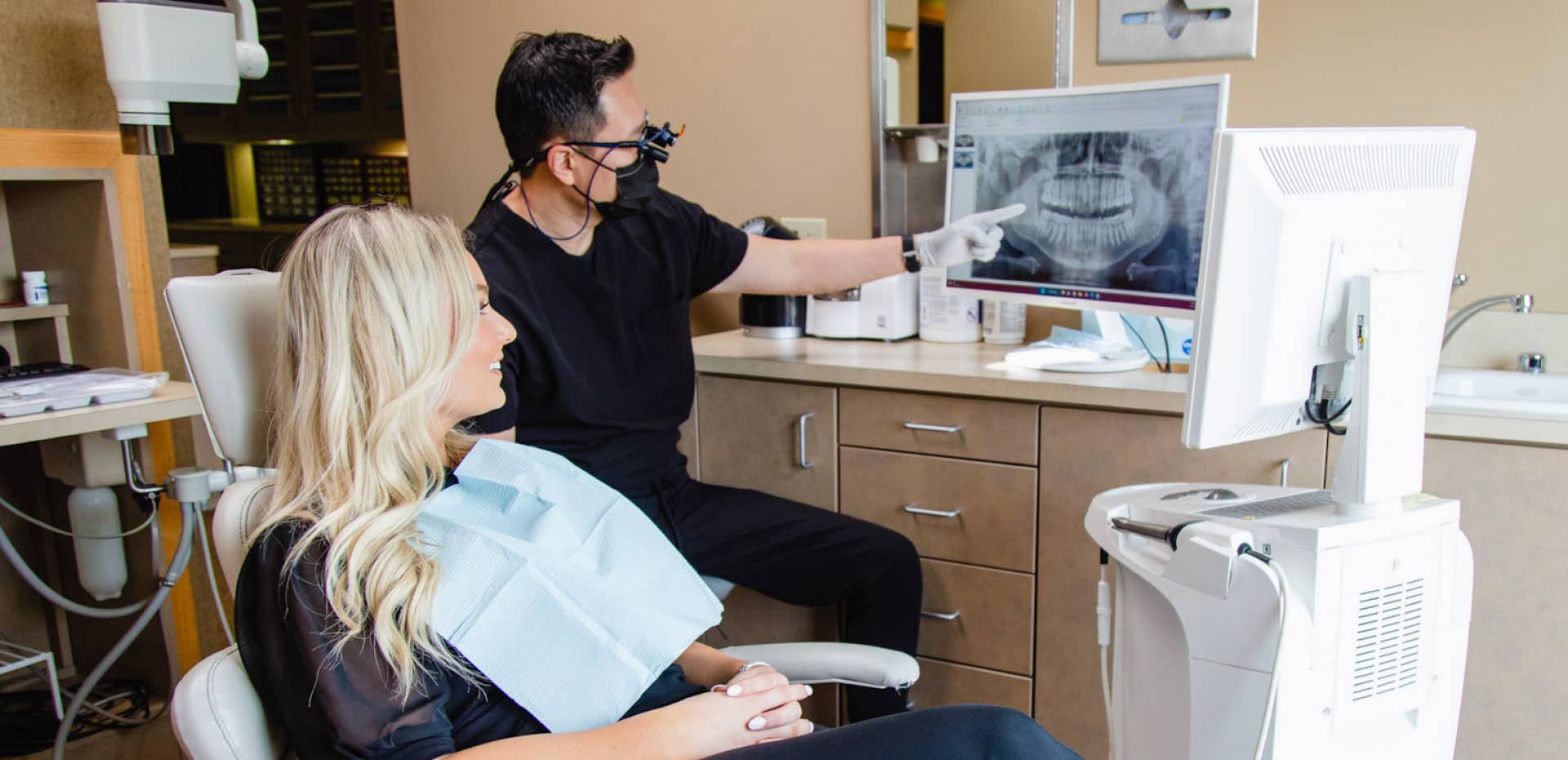Dr. Sim pointing to dental x-ray on computer monitor sitting next to patient in dental chair