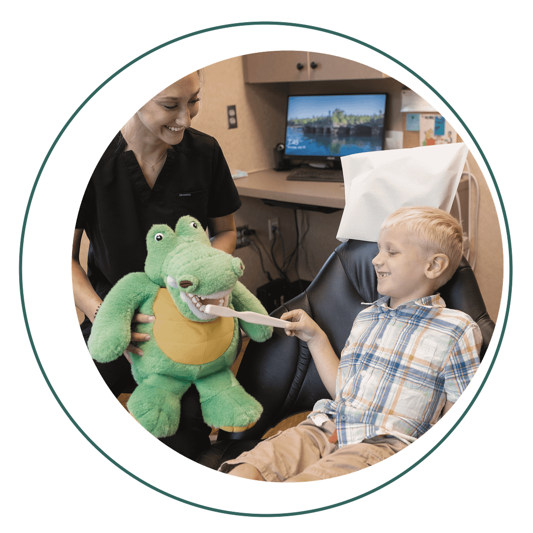 assistant showing pediatric patient how to brush teeth using stuffed alligator