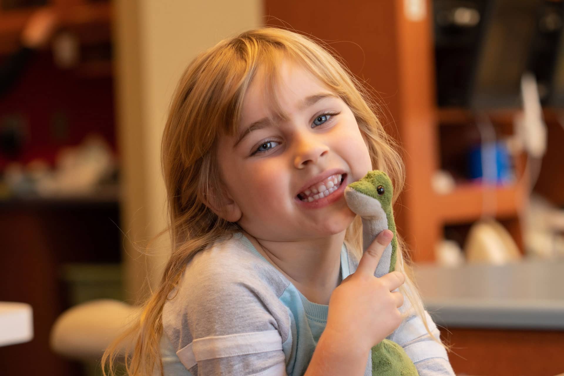 young girl smiling and holding stuffed dinosaur