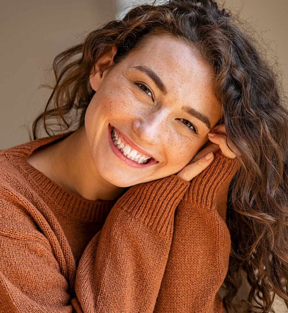 young smiling woman with curly hair wearing orange sweater