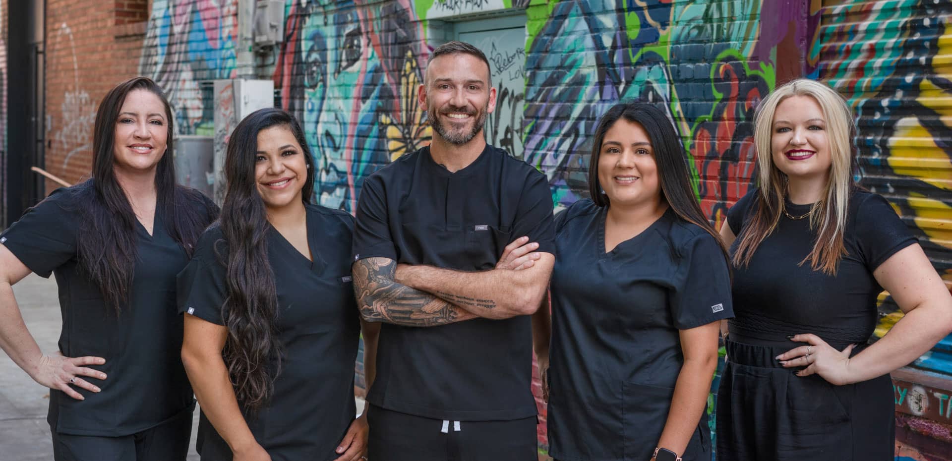 Dr. Williams with Bold Dental team members wearing black scrubs standing in front of a brick wall with colorful graffiti